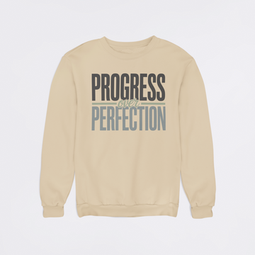 Beige sweatshirt with 'Progress Over Perfection' text on a light gray background